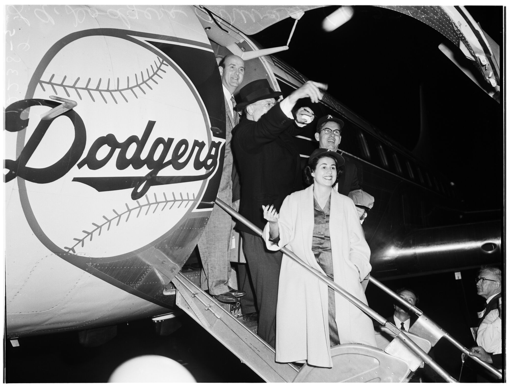 Walter O'Malley throwing out a baseball while descending airplane stairs as a woman watches.