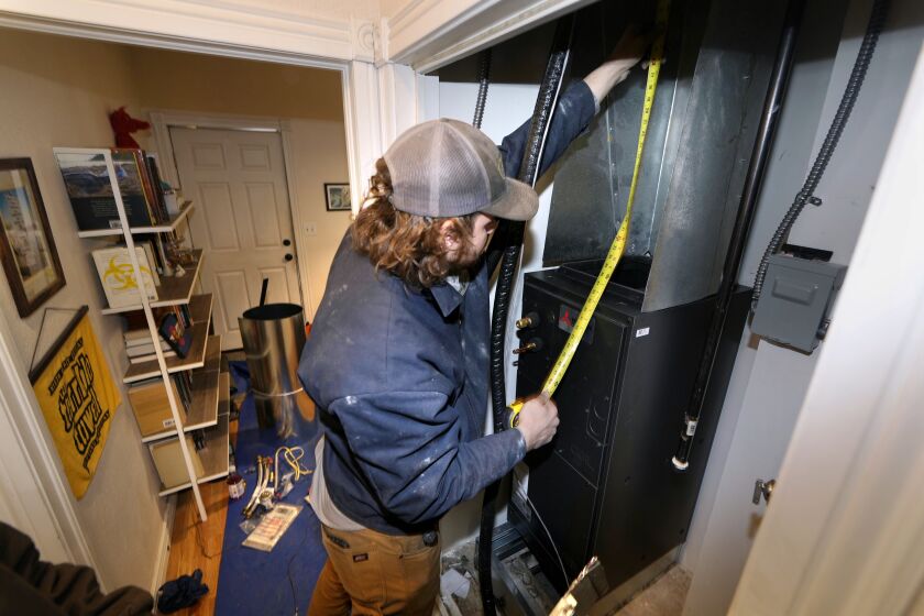 John Paul uses a tape measure during the installation of a heat pump in an 80-year-old rowhouse Friday, Jan. 20, 2023, in northwest Denver. (AP Photo/David Zalubowski)