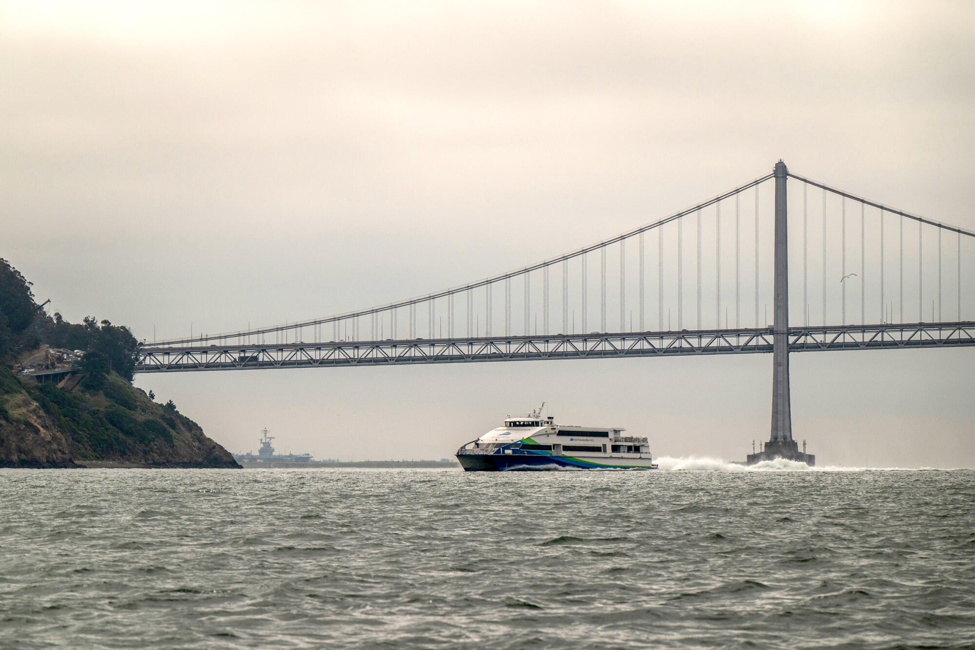 A high-speed ferry motors through San Francisco Bay under overcast skies.