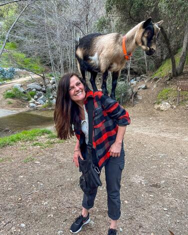 A woman with a goat on her back on a hike.  