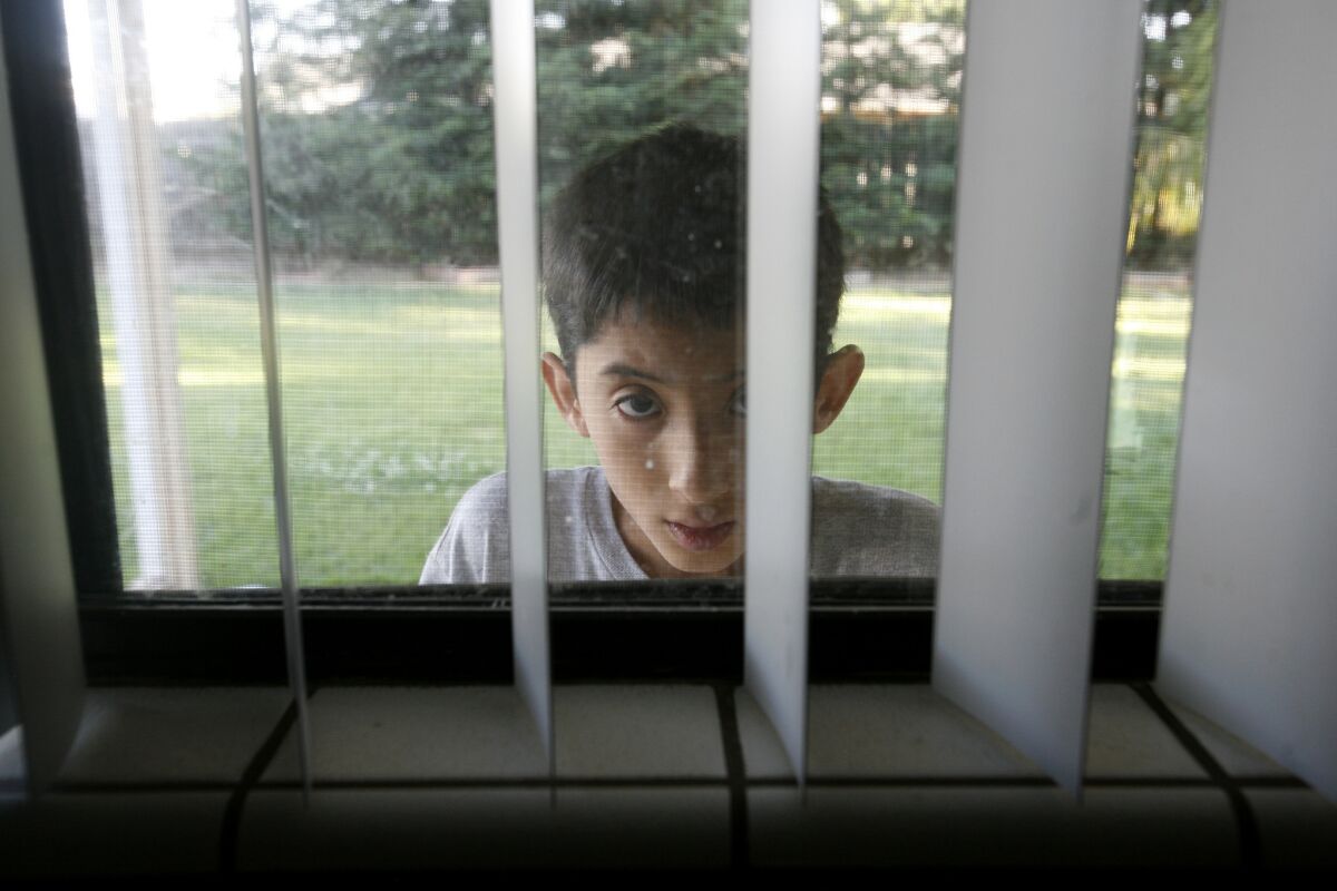 Joseph Gutierrez, 13, peeks into his kitchen window in Sanger, Calif. He has been diagnosed as mentally retarded, but his mother thinks he is autistic.