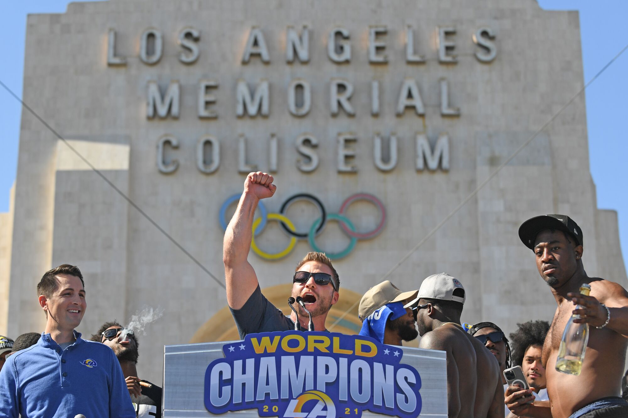 Rams coach Sean McVay raises his arm at a lectern in front of the Coliseum.