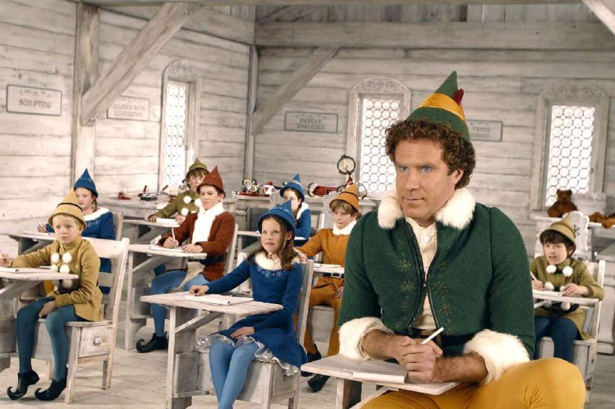 An oversize elf sits at a desk in a classroom filled with normal-size elves at desks.