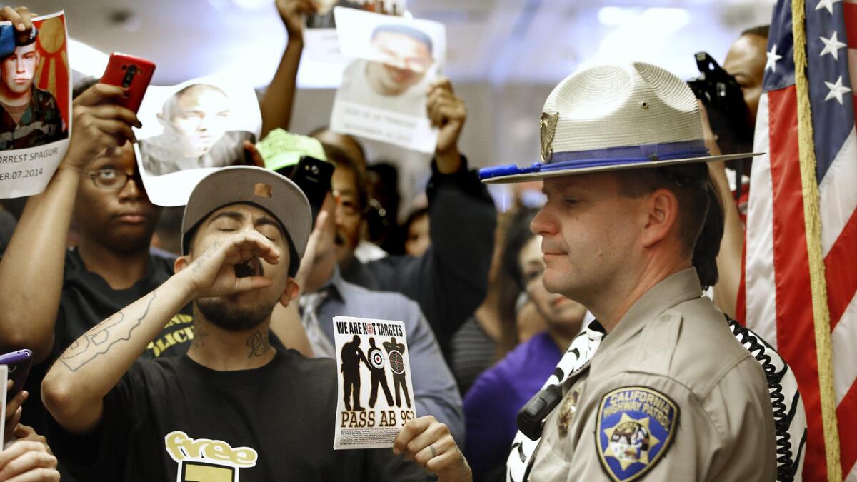 A California Highway Patrol officer stands outside the office of Gov. Jerry Brown in 2015 as protesters shouting "black lives matter" demand passage of racial profiling legislation.
