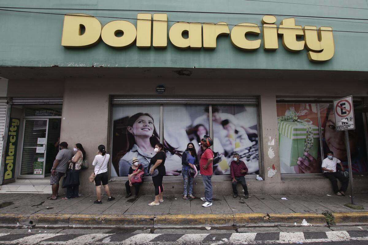 Compradores usando mascarillas de protección están formados afuera de Dollarcity en San Salvador