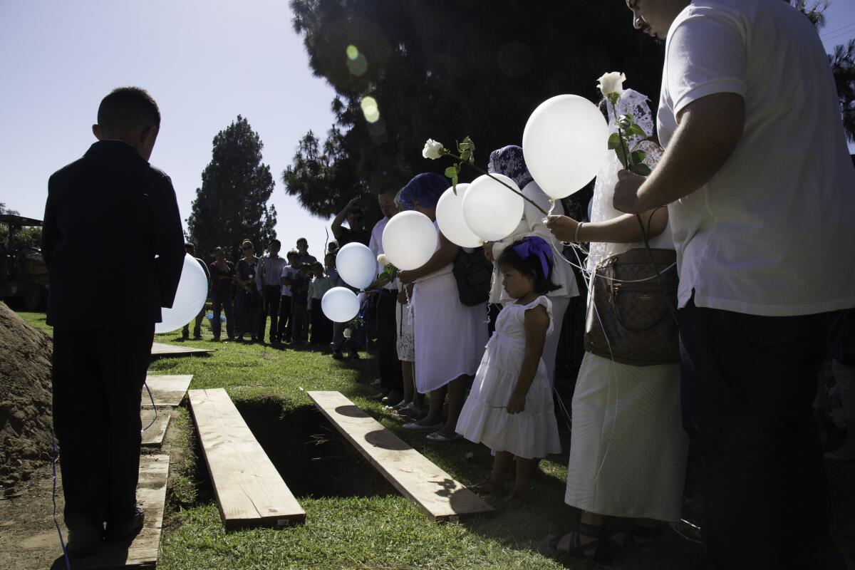 People with white balloons stand around a gravesite