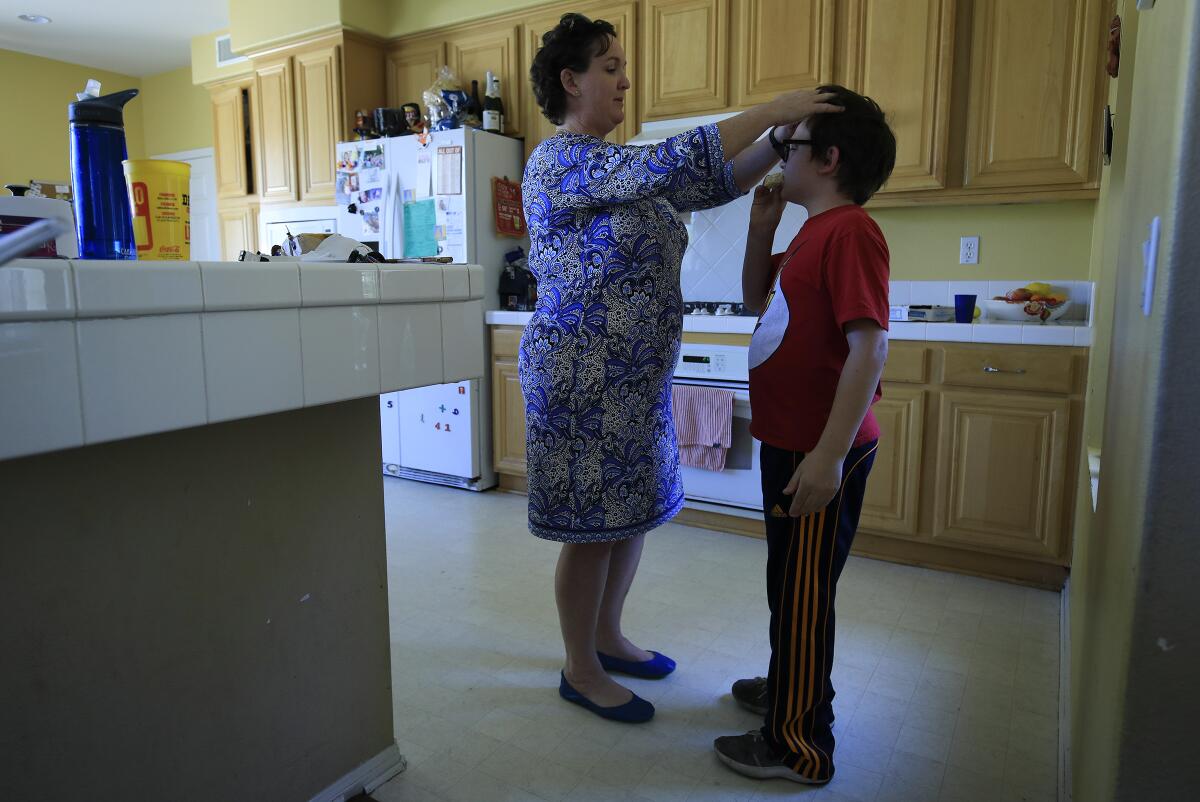 Katie Porter with her hands on the head of her young son in their kitchen.