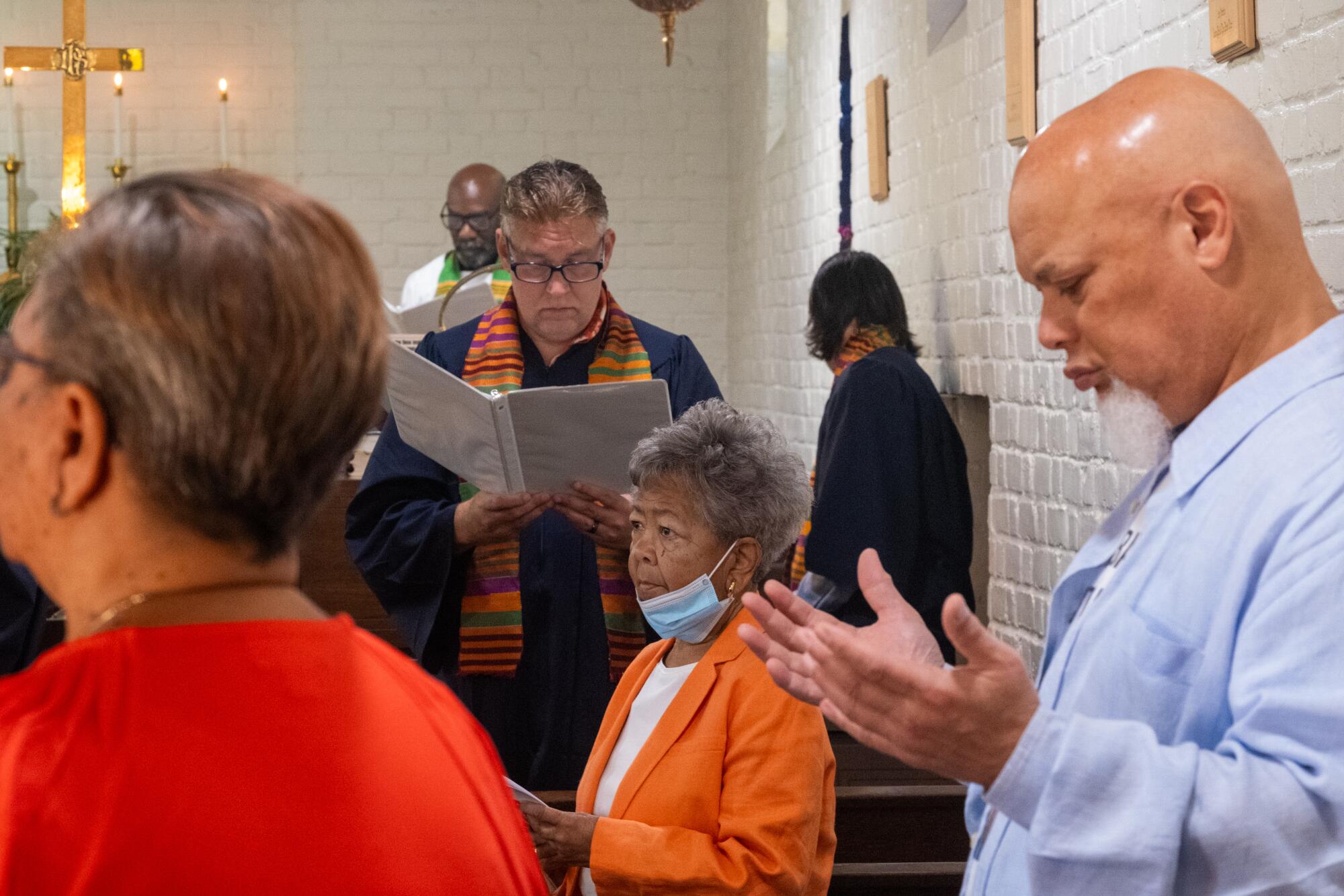 A woman, surrounded by other people, stands at the center of pews of a small church 