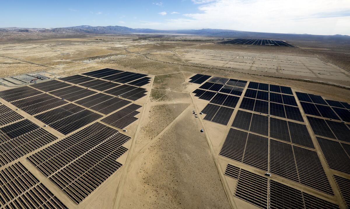 An aerial view of rows of solar panels on a dry plain.