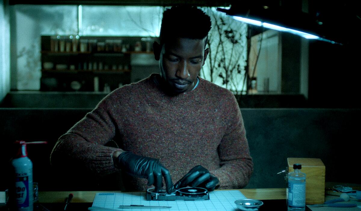 A man wearing a sweater and black gloves looks down as he works on a tape.