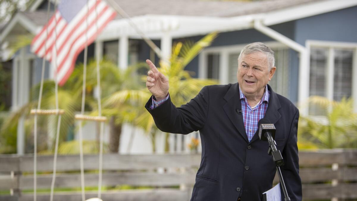 Rep. Dana Rohrabacher points to a commercial aircraft that could be heard leaving nearby John Wayne Airport during a news conference Monday outside his Costa Mesa home.