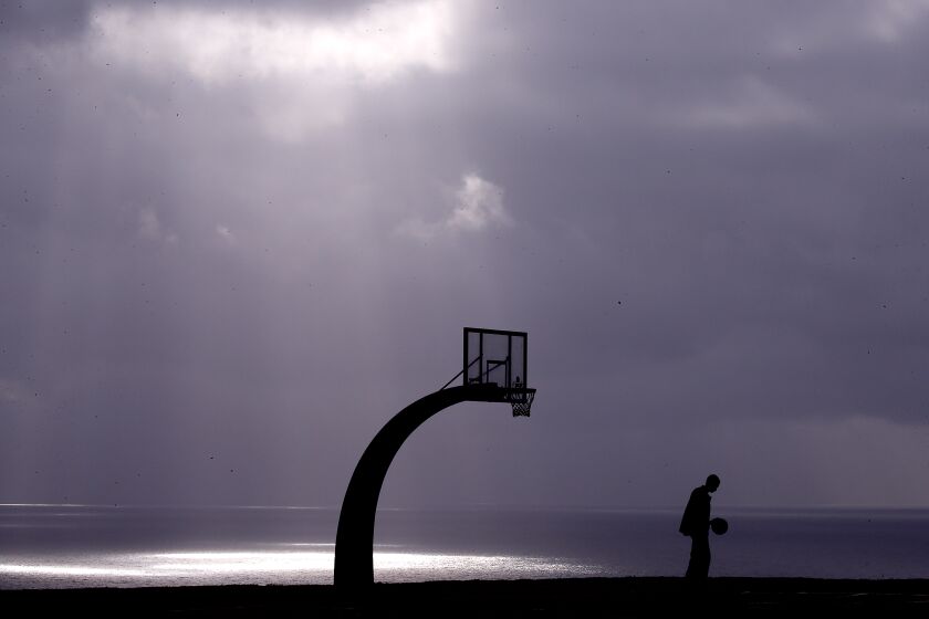 A lone man sits near a basketball court on a coast.