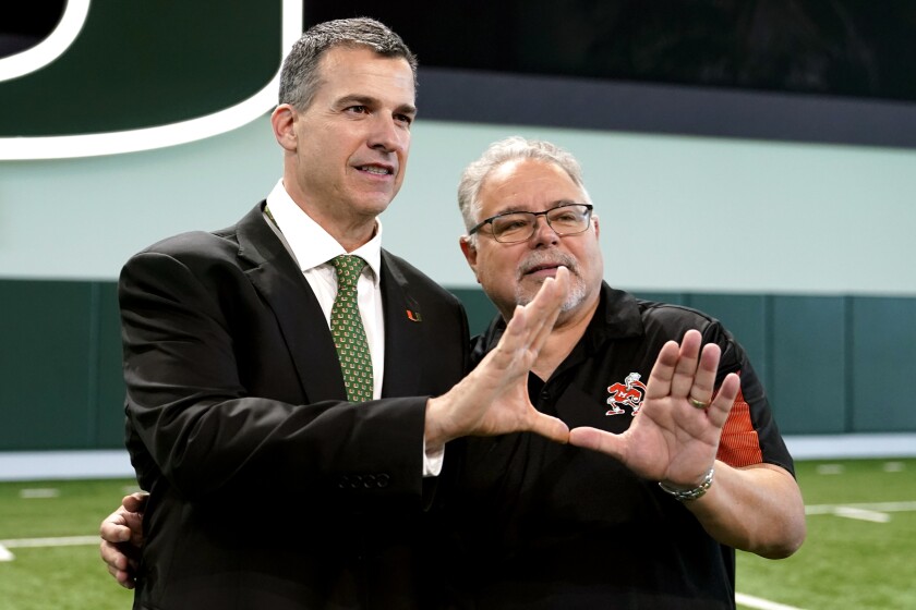 Mario Cristobal, left, Miami's new football coach, makes the sign of the "U" with Harry Rothwell, right, after being introduced at a NCAA college football news conference, Tuesday, Dec. 7, 2021, in Coral Gables, Fla. Cristobal is returning to his alma mater, where he won two championships as a player. Rothwell is a local businessman and Hurricanes fan. (AP Photo/Lynne Sladky)