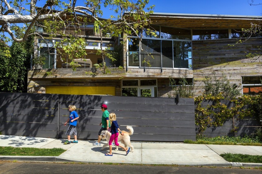 Neighbors and their dog walk past the Soffer-Adler home in Rustic Canyon, designed by L.A. architect Peter Kim. The exterior of the home is wrapped in reclaimed snow-fence wood from Wyoming. Petrified lichen on the siding adds a touch of green. A century-old sycamore stands at left.