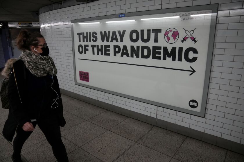 A woman wearing a face mask to curb the spread of coronavirus walks past a health campaign poster from the One NGO, in an underpass leading to Westminster underground train station, in London, Thursday, Jan. 27, 2022. Most coronavirus restrictions including mandatory face masks were lifted in England on Thursday, after Britain's government said its vaccine booster rollout successfully reduced serious illness and COVID-19 hospitalizations. From Thursday, face coverings are no longer required by law anywhere in England. (AP Photo/Matt Dunham)