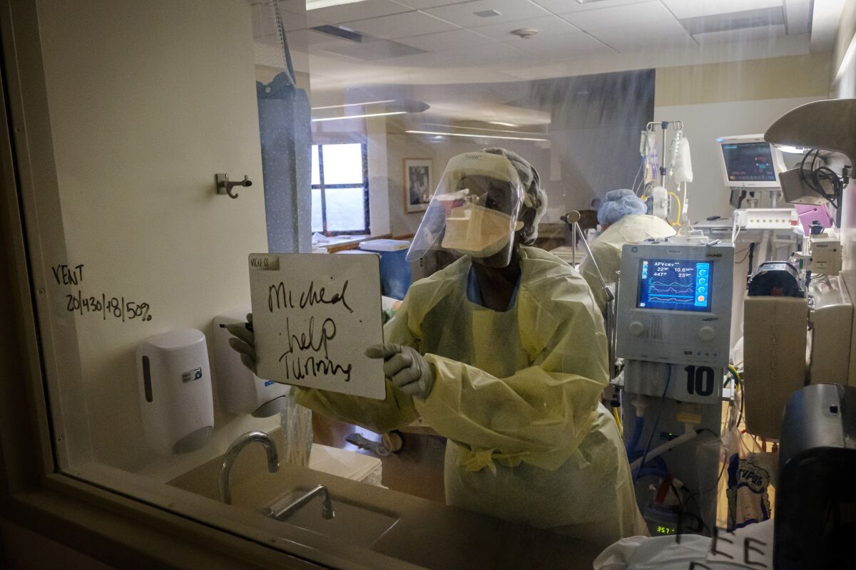 Registered Nurse Linda Isidienu signals for her co-worker Michael Manriquez to come help with a patient diagnosed with COVID-19 and placed on a ventilator inside a negative- pressure isolation room at the Intensive Care Unit at Sharp Chula Vista Medical Center on April 10, 2020.