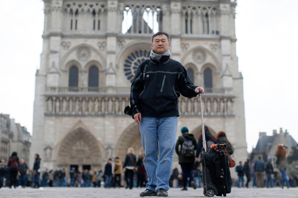 A man holds the extension handle of a small suitcase while standing.