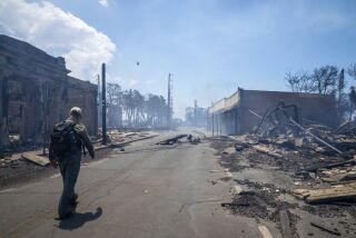 A man walks past wildfire wreckage on a city street