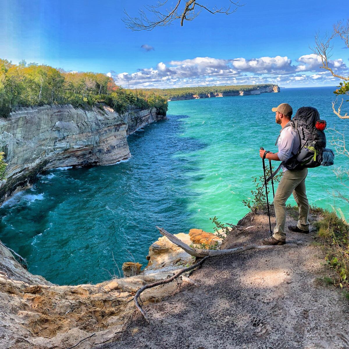A man with hiking gear stands atop a cliff with a view of Lake Superior.