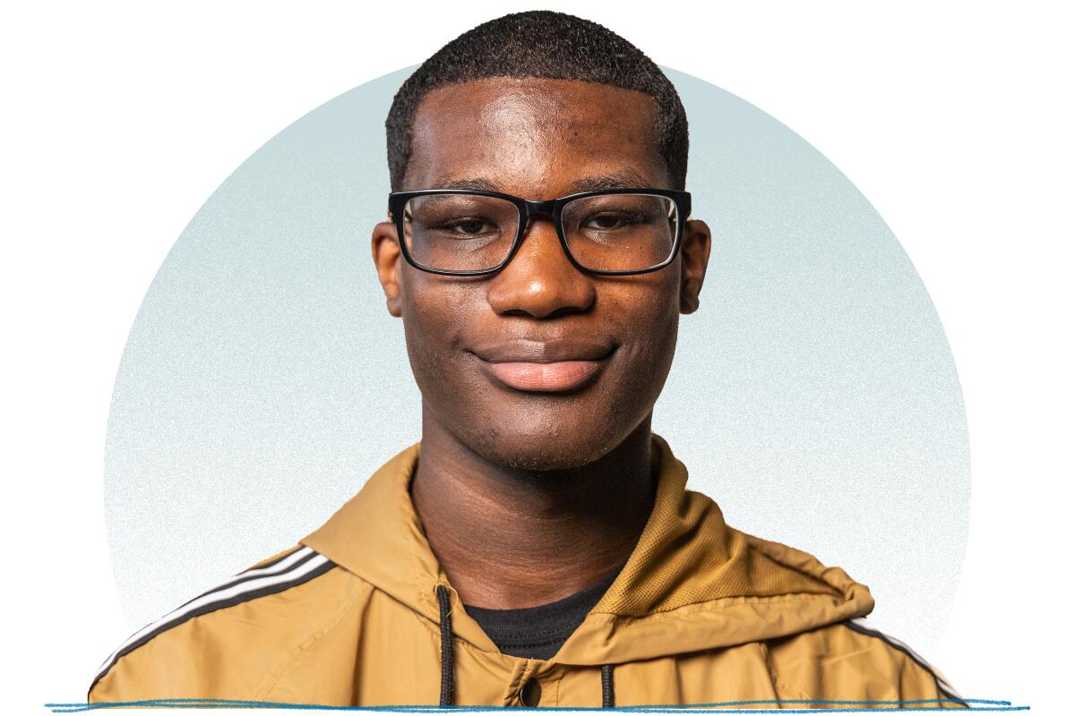 A young man with black buzzed hair wearing rectangular black glasses smiling for a portrait.