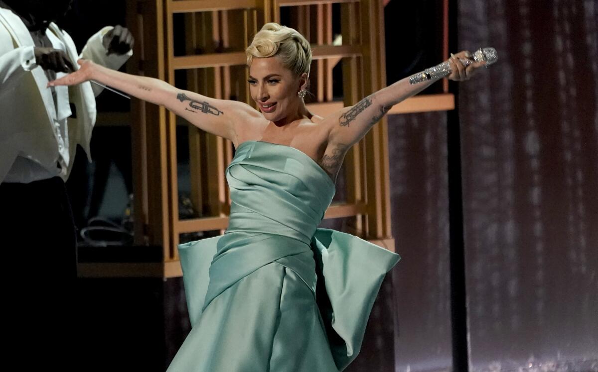 A blonde woman with a turquoise dress and tattoos performs at an awards ceremony