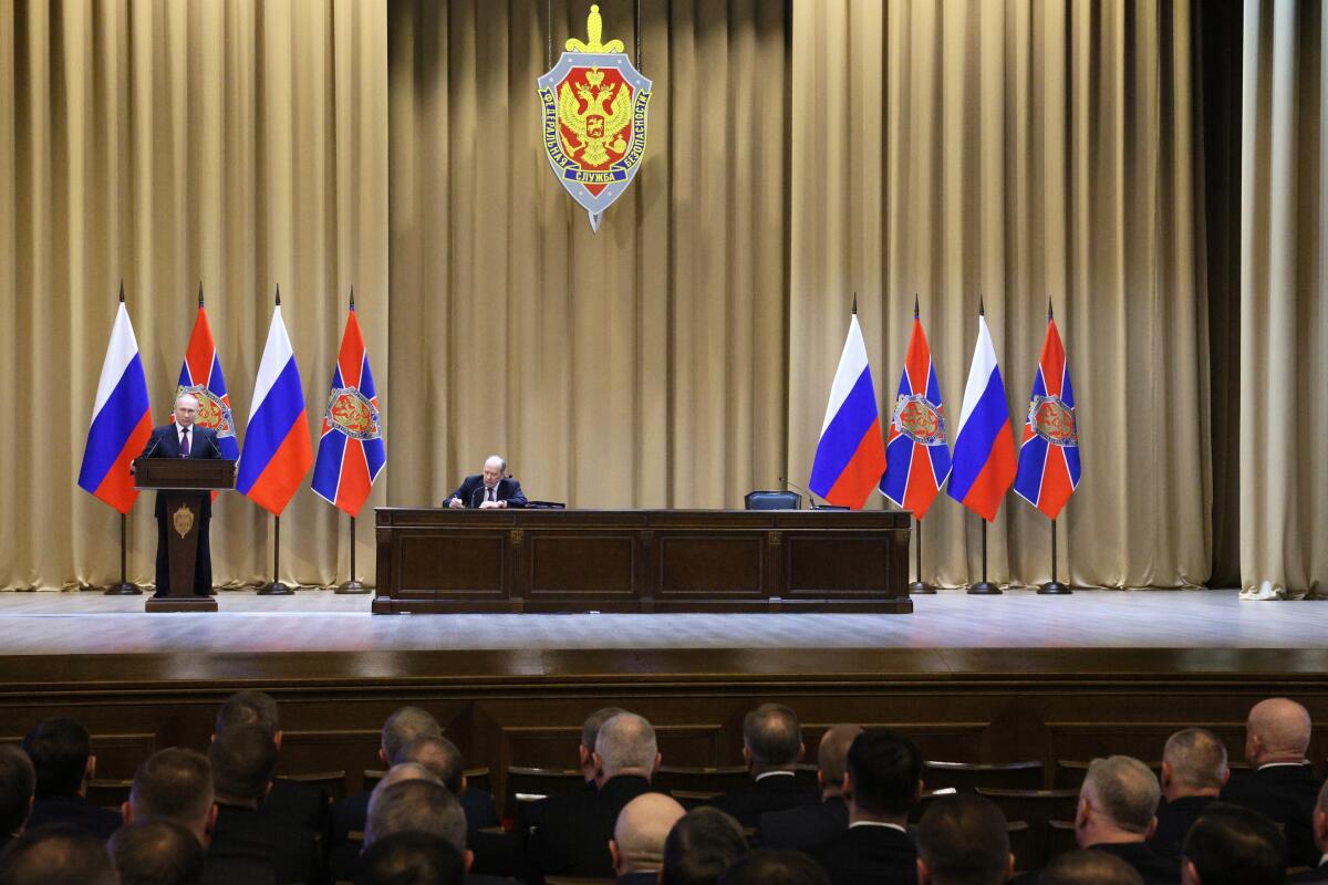Russian President Vladimir Putin speaks on a stage decorated with Russian flags.