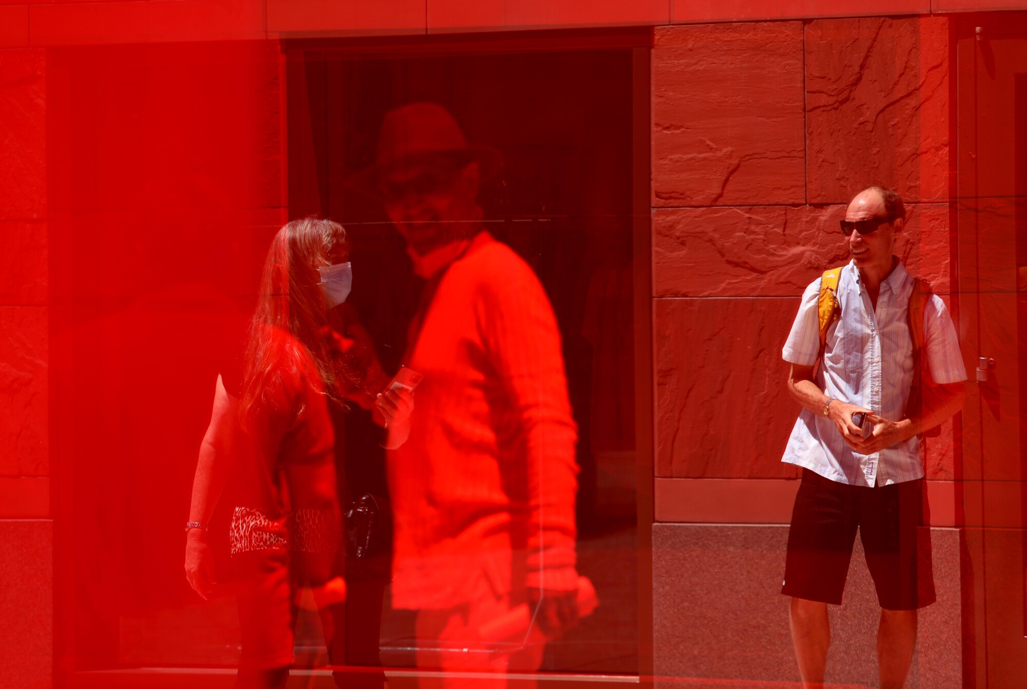 People are reflected on a red surface.