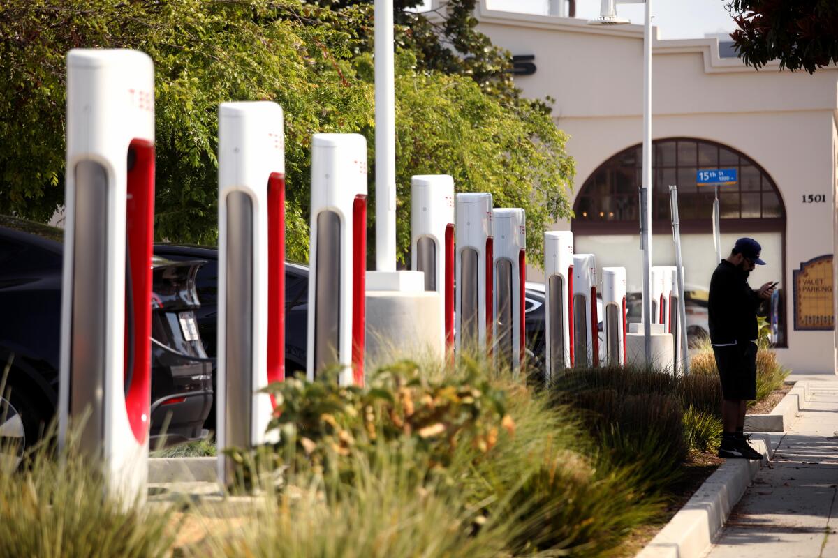 A man stands next to a row of charging towers at a Tesla Supercharger station.