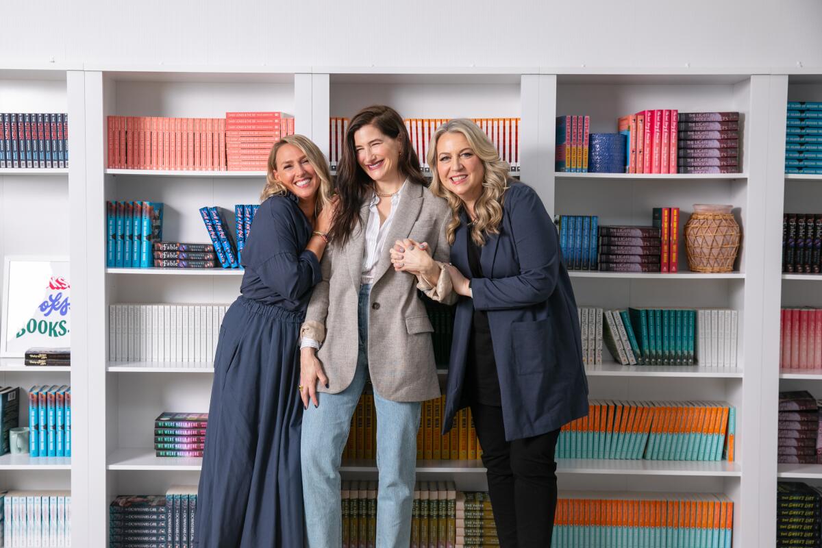 Three women (showrunner Liz Tigelaar, actress Kathryn Hahn and author Cheryl Strayed) smile together in front of books.