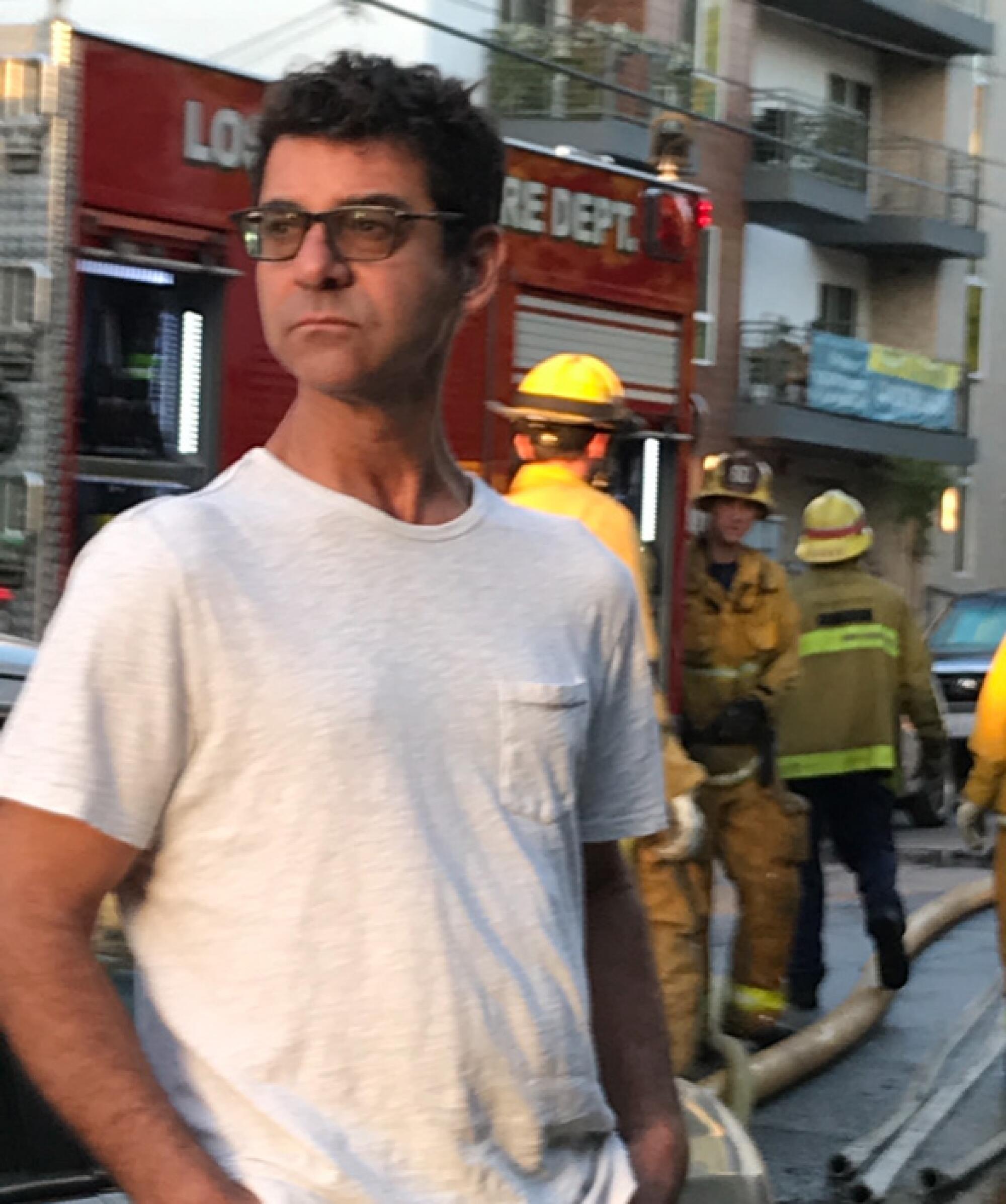 A man stands by a fire truck and fire fighters