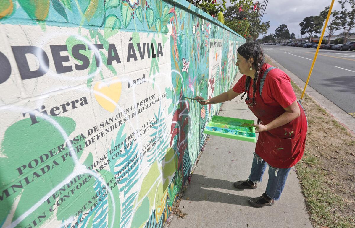 Artist Alicia Rojos paints over the vandal's spray-painted words "white power" on the Poderosas mural wall.