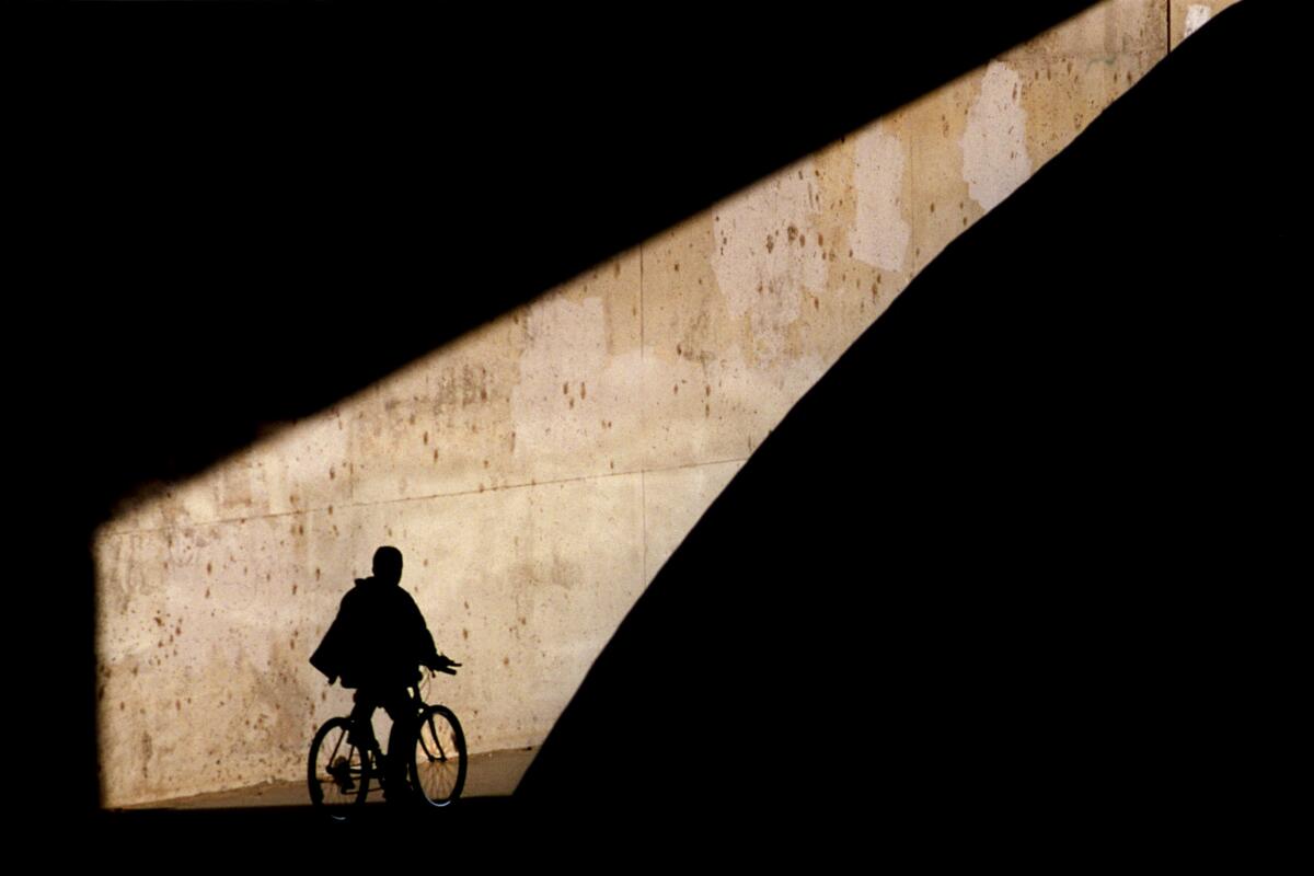 A bicyclist in shadow, highlighted by a shaft of light.