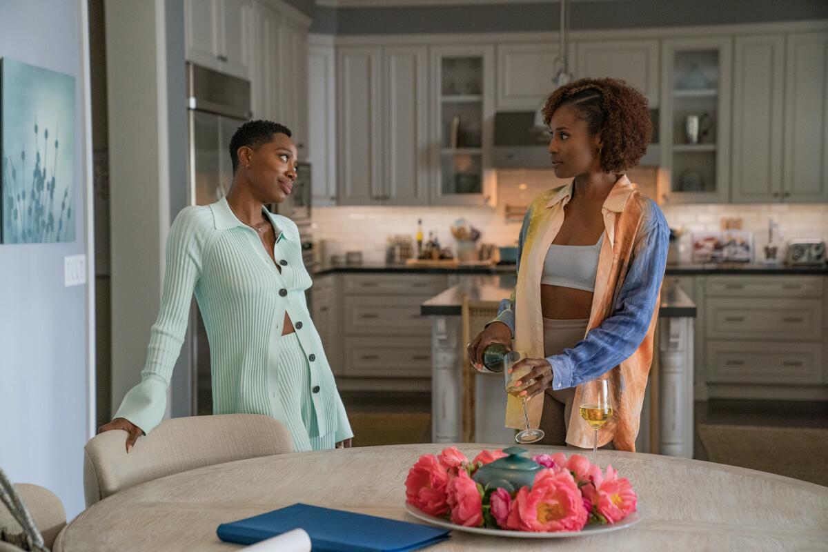 Two women stand by a table talking in a scene from "Insecure."