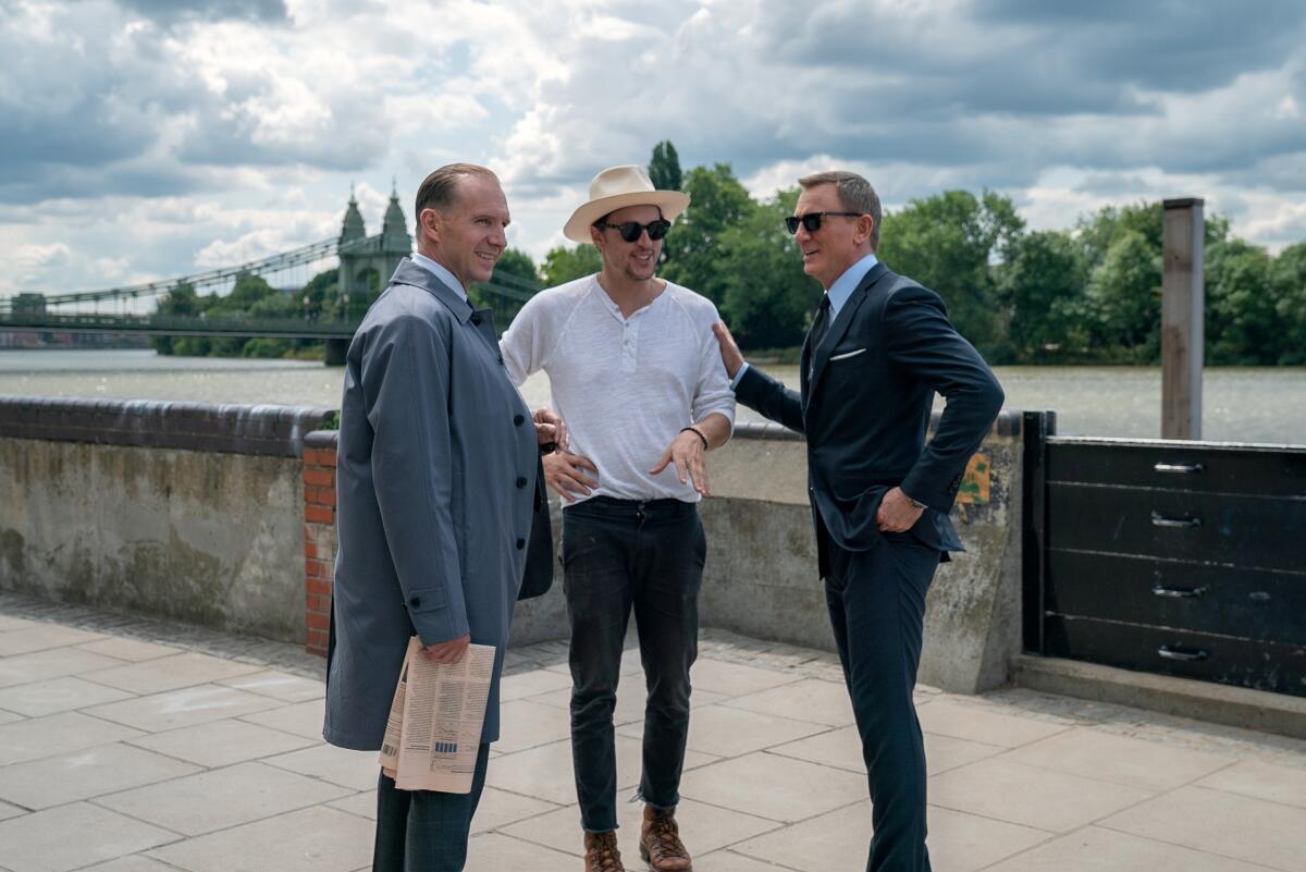 Ralph Fiennes (as M), director Cary Joji Fukunaga and Daniel Craig (as James Bond) smiling near a bridge.