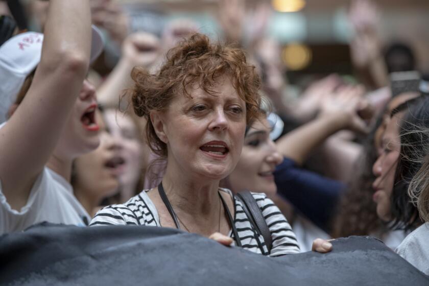 Susan Sarandon standing in large crowd, protesting with others, holding a banner