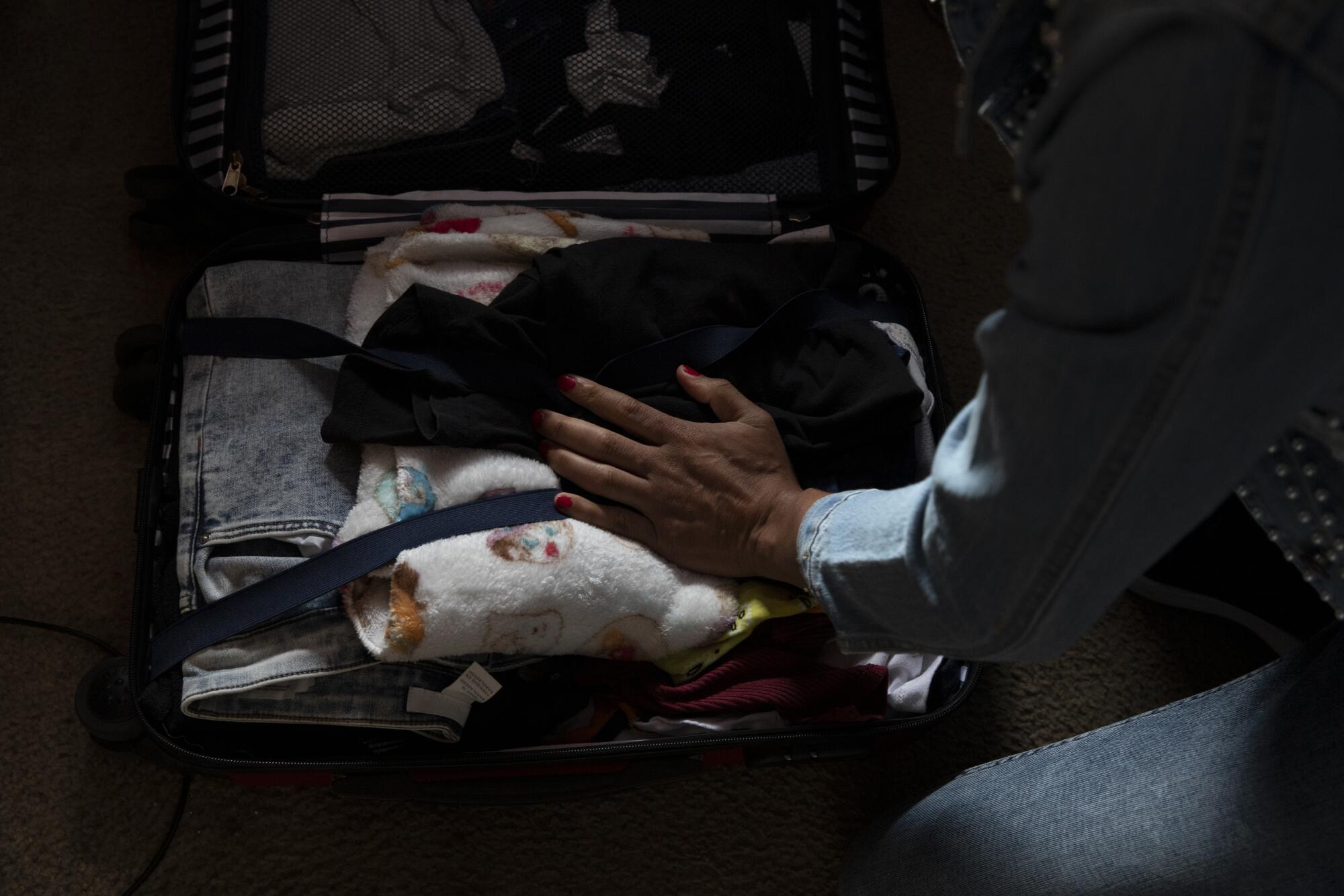 Ceidy Zethare's manicured hand is visible adjusting items in her suitcase