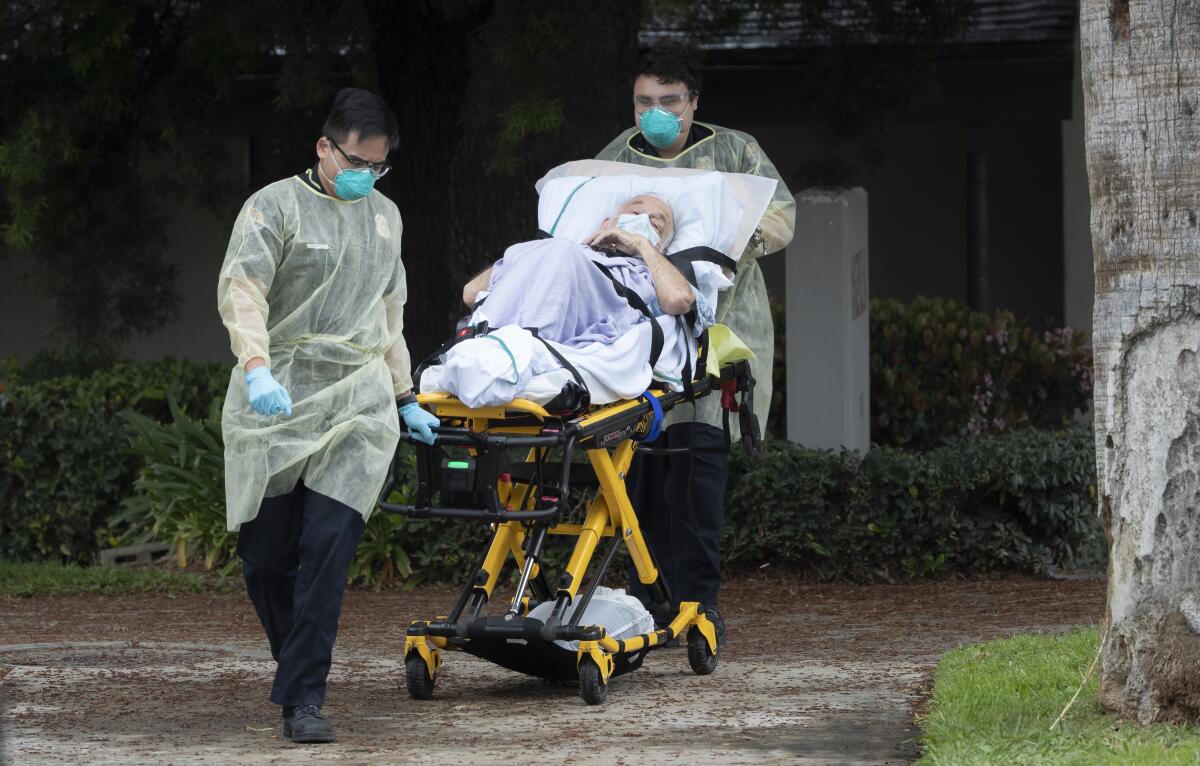 Two men in masks and gowns wheel a person out on a gurney