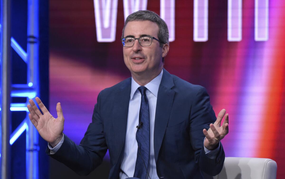 John Oliver seated before a colorful background.
