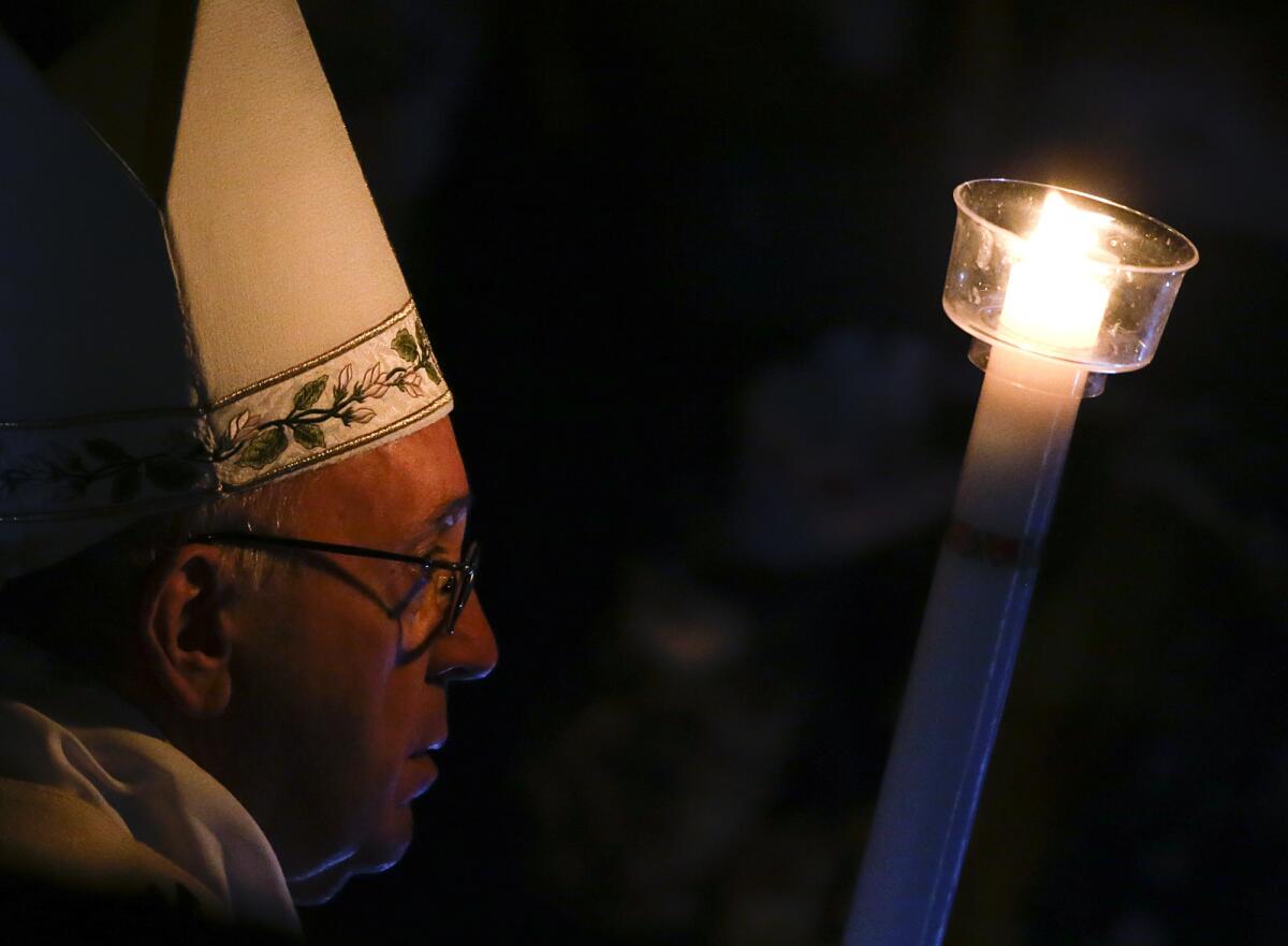 Pope Francis holds a white candle as he arrives for an Easter vigil service at St. Peter's Basilica, at the Vatican.