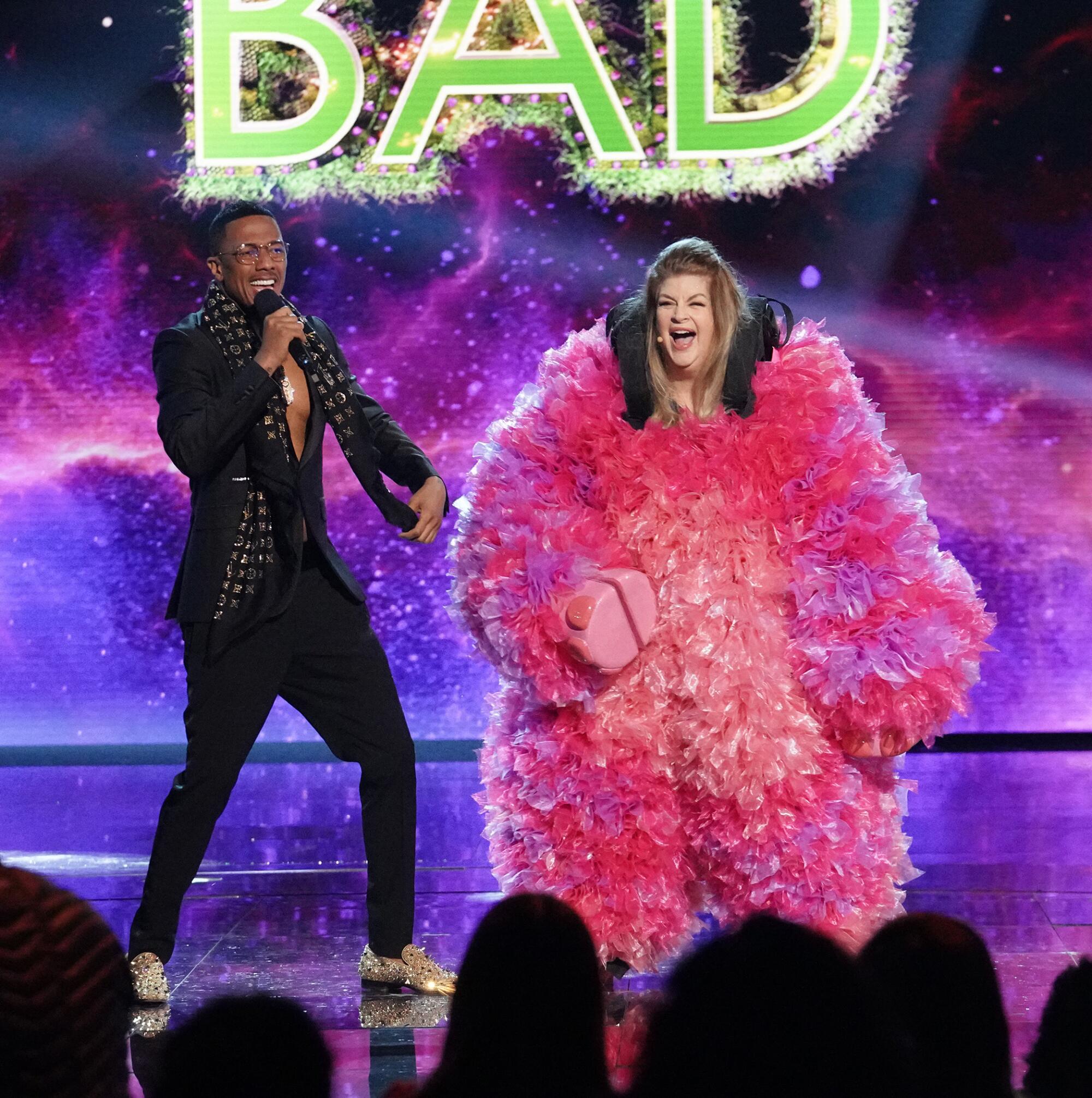 A man holding a microphone stands next to a woman wearing a fluffy pink costume on stage