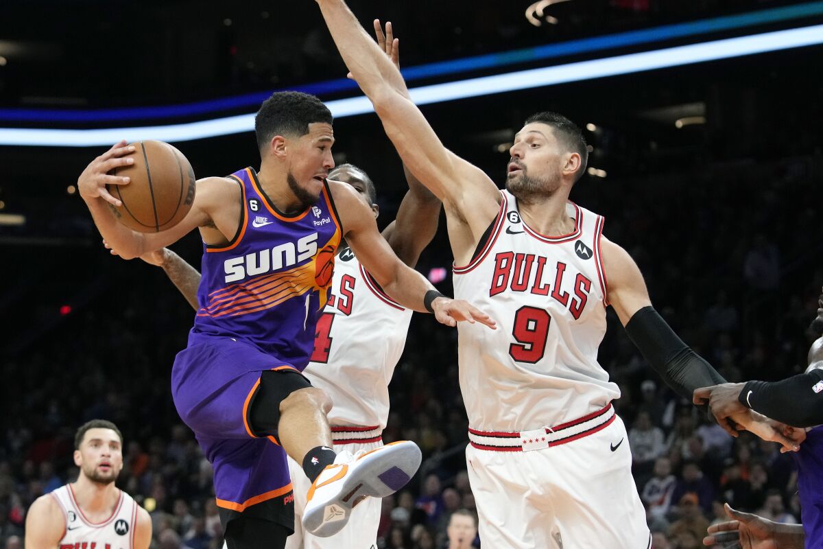 Phoenix Suns guard Devin Booker (1) is stopped on a drive to the basket by Chicago Bulls center Nikola Vucevic (9) and Bulls forward Patrick Williams, second from right, as Bulls guard Zach LaVine, left, looks on during the first half of an NBA basketball game in Phoenix, Wednesday, Nov. 30, 2022. (AP Photo/Ross D. Franklin)