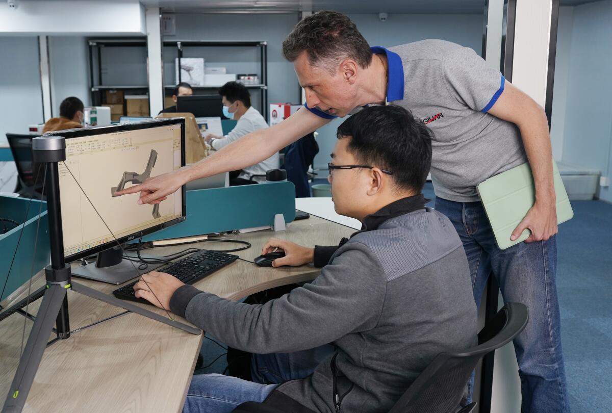 Two men, one sitting and one standing, look at a computer screen.