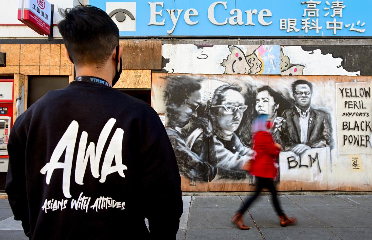 A man looks at a mural painted on plywood of activists and the words "Yellow peril supports Black power"