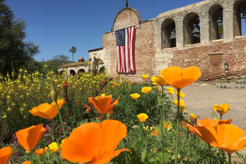 Mission San Juan Capistrano with a U.S. flag and California poppies.