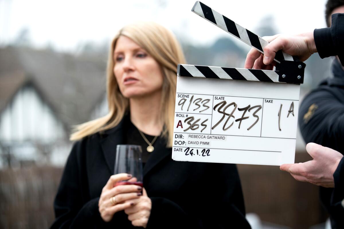 A woman dressed in black, holding a glass, behind a film slate