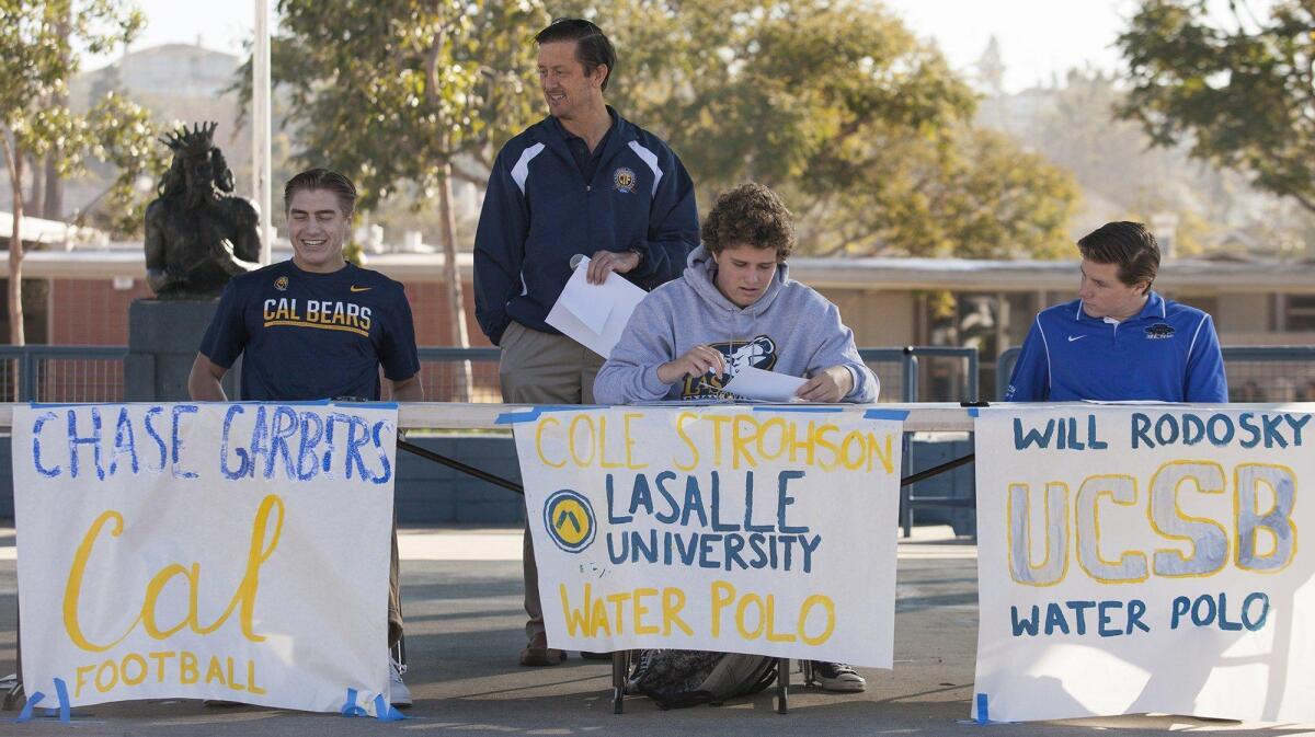 Corona del Mar High School athletic director Don Grable, standing, shares a laugh with Chase Garbers, left, after handing him, Cole Strohson, center, and Will Rodosky their letters of intent during National Letters of Intent for college on Wednesday.