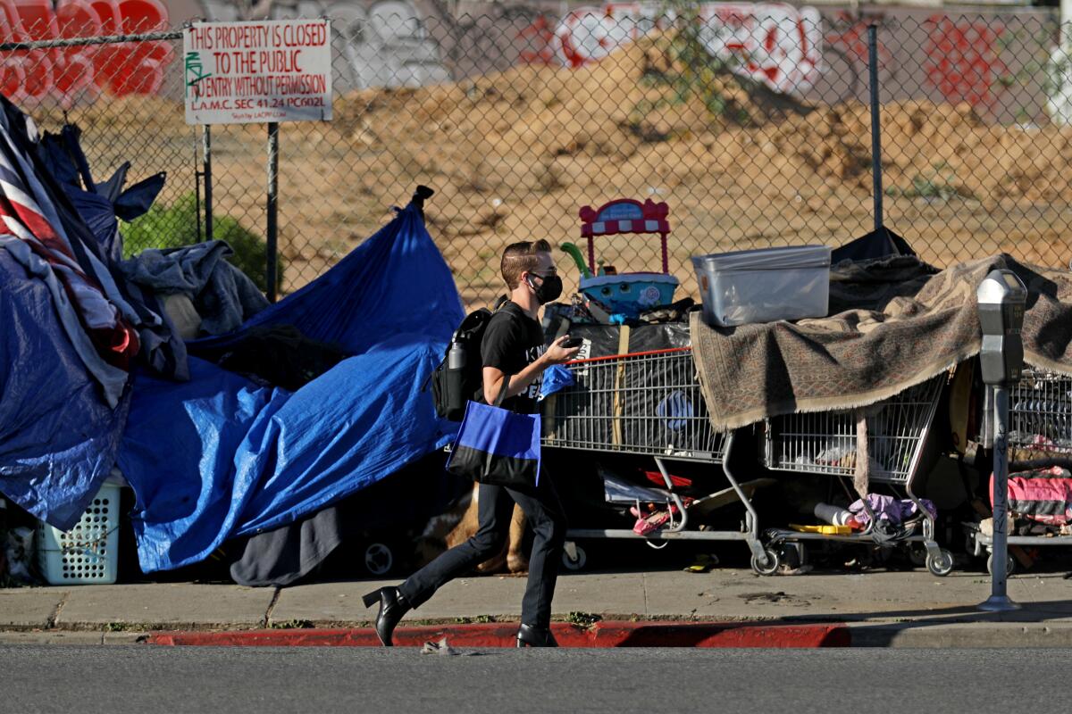 A pedestrian walks past a homeless encampment on the sidewalk.