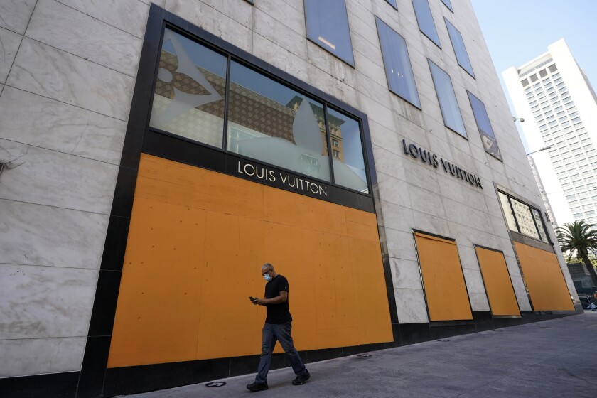 A man walks past a boarded-up Louis Vuitton store.