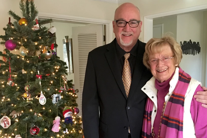 Bill Plaschke stands next to a Christmas tree with his arm around his mother, Mary Margaret Plaschke