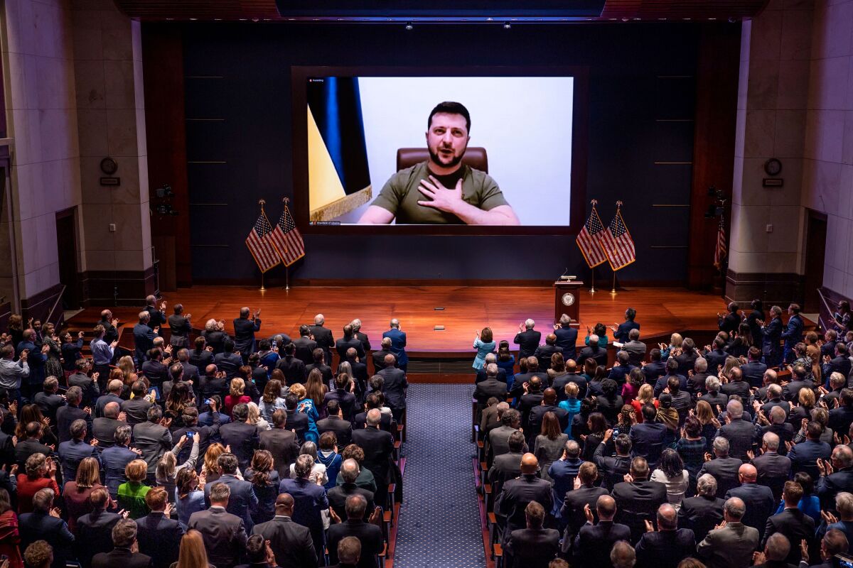 Ukrainian President Volodymyr Zelensky, seated, with his hand over his heart, on a video screen before members of Congress